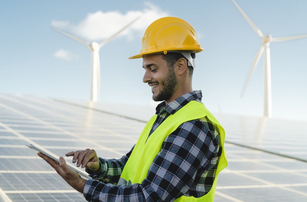 Young engineer watching on tablet the green plan for alternative energy with turbine and solar panel